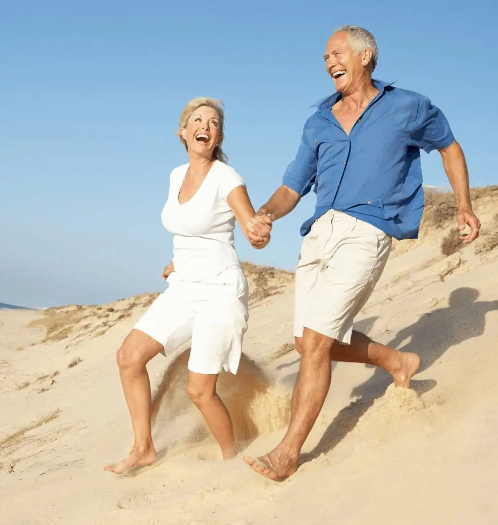 Smiling older couple running barefoot on sand